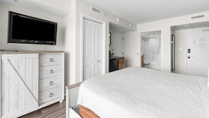 Un dormitorio con una cama grande, un televisor montado en la pared, un aparador de madera y una puerta que da a un baño.