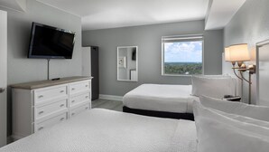 A hotel room with two beds, a TV, a dresser, a window with a view, and a lamp. - Seaside Splendor 2 Balcony Suite with Sunset Views (Myrtle Beach)