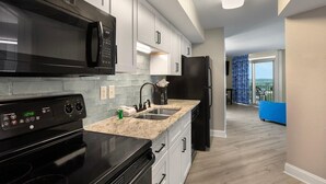 A modern kitchen with white cabinets, a black microwave, a black refrigerator, and a stainless steel sink. - Seaside Splendor 2 Balcony Suite with Sunset Views (Myrtle Beach)