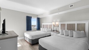 Quarto de hotel com duas camas, uma escrivaninha, televisão e janela com cortinas.
