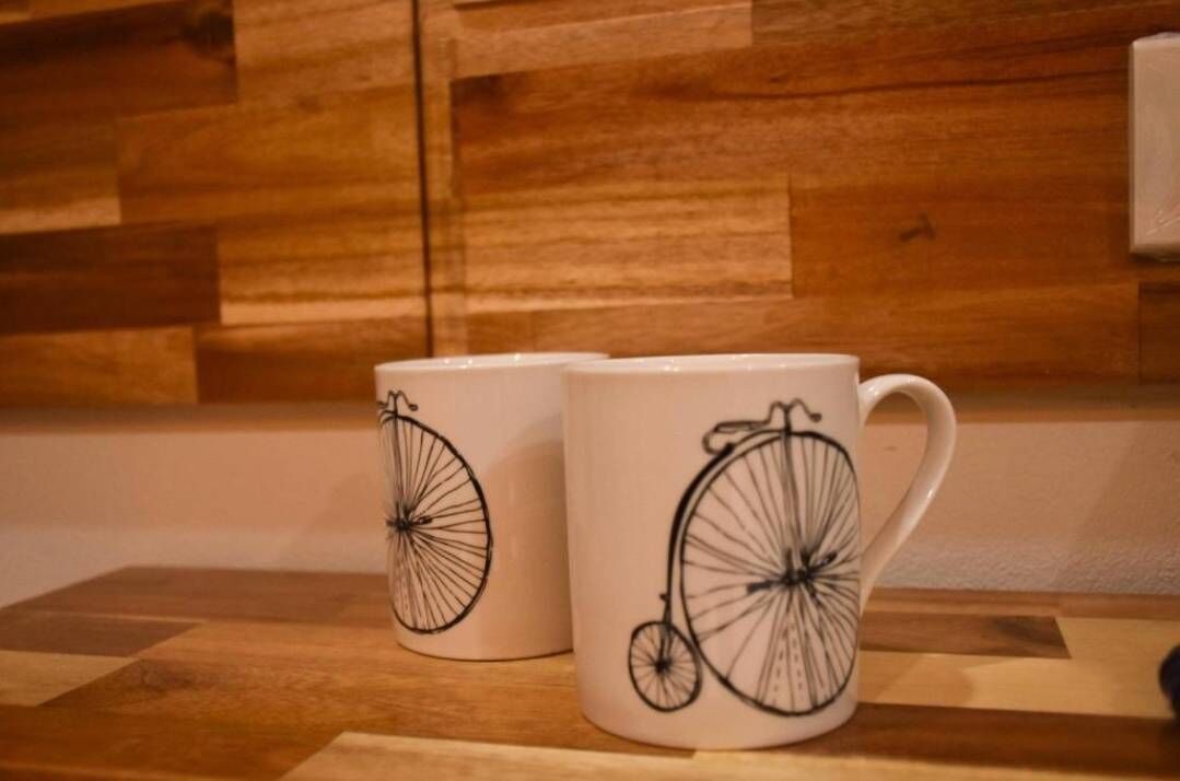 Deux tasses blanches ornées de motifs de vélos noirs, posées sur une surface en bois.