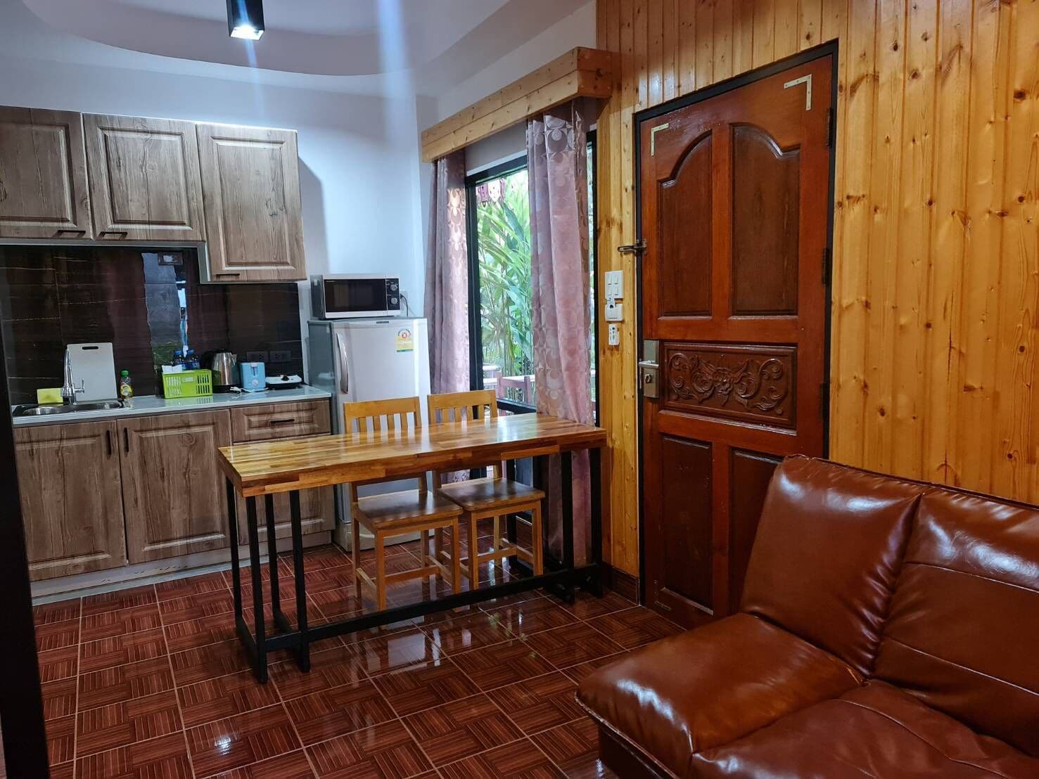 Une cuisine compacte avec des meubles en bois, un four à micro-ondes et un réfrigérateur. On y trouve une table à manger avec des chaises et un canapé en cuir.