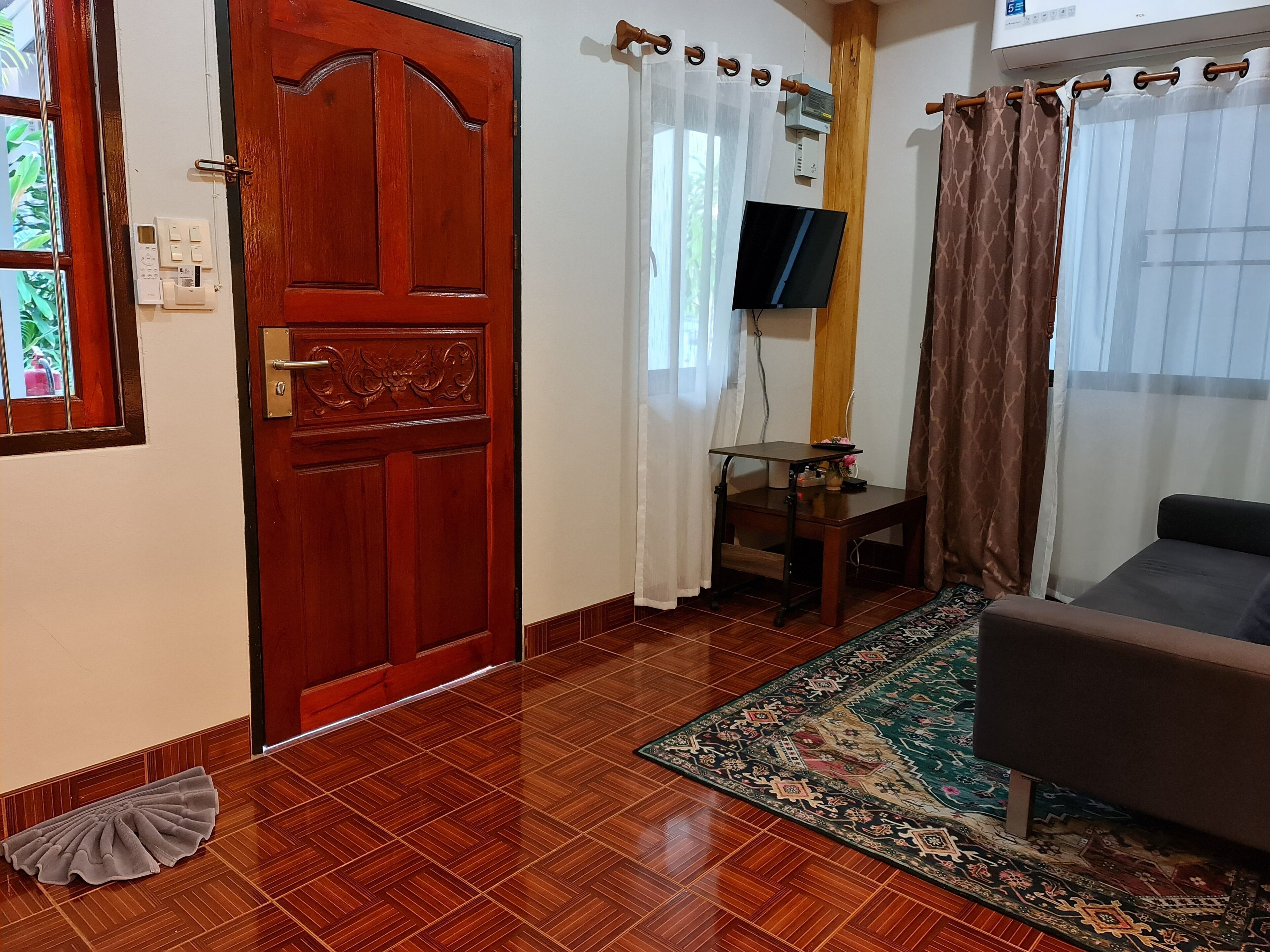 Una habitación con puerta de madera, televisor en la pared, una mesita, un sofá y una alfombra estampada.