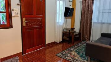 Una habitación con puerta de madera, televisor en la pared, una mesita, un sofá y una alfombra estampada.
