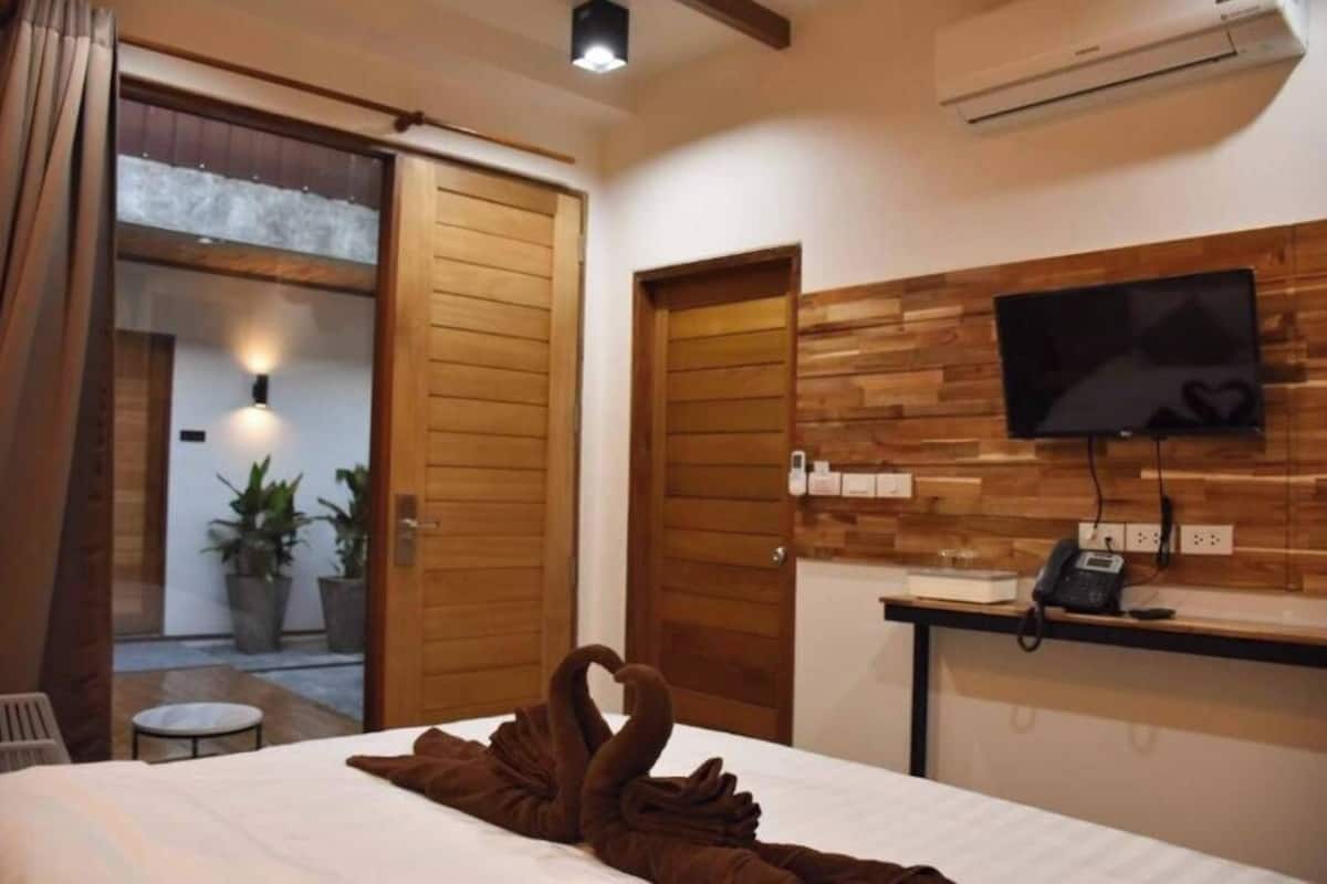 Ein Hotelzimmer mit Bett, Wandfernseher, Schreibtisch mit Telefon und einer Holzvertäfelung.