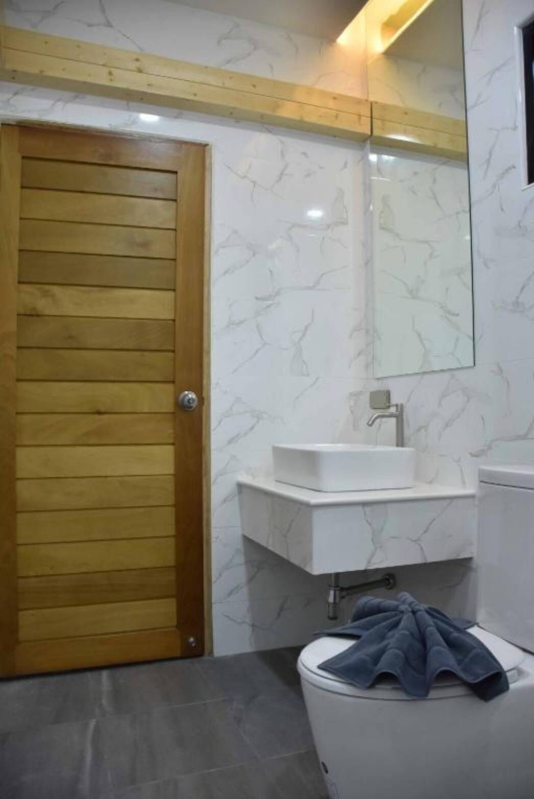 A bathroom with a wooden door, a white sink, a mirror, and a toilet.