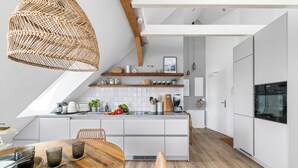 Een moderne keuken met witte kasten, een houten eettafel en een hangende rotanlamp.