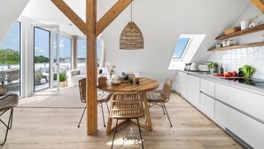 Een moderne keuken met houten balken, een ronde eettafel, rieten stoelen en een hanglamp.