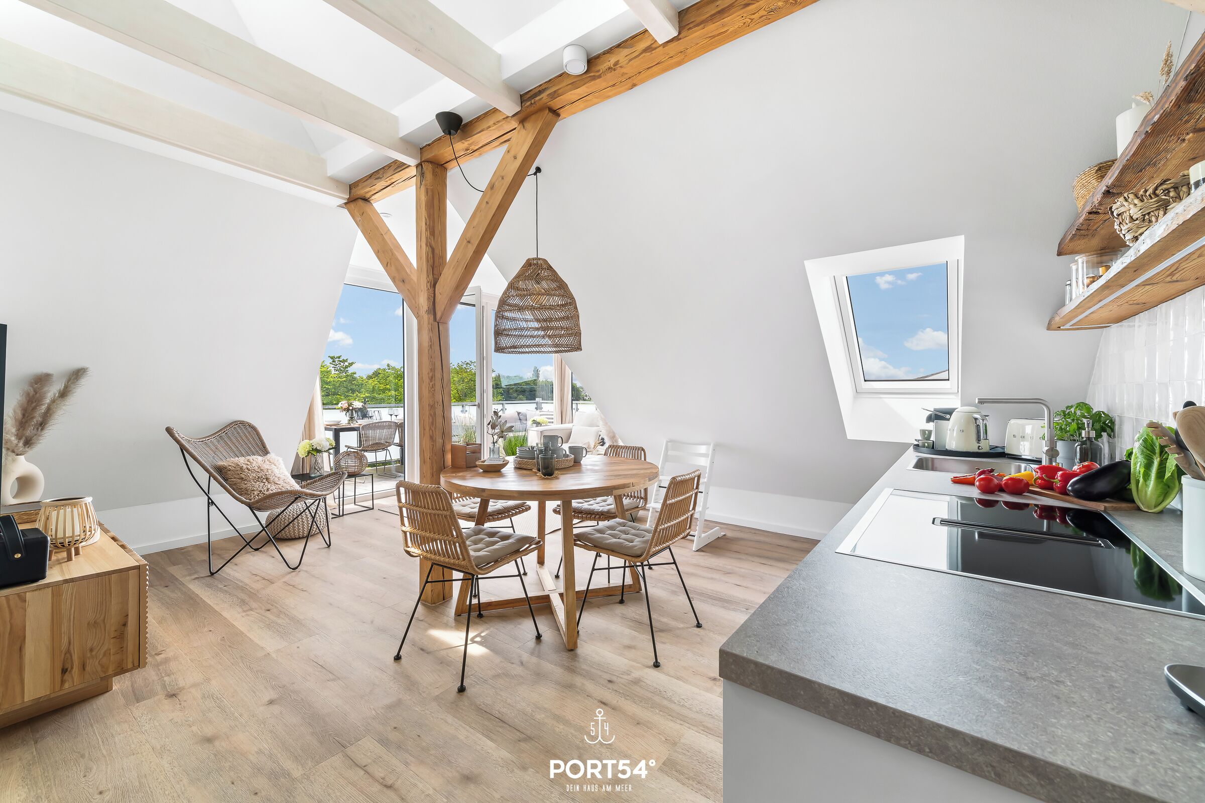 Eine moderne Küche mit einem runden Holztisch, Korbstühlen und einem großen Fenster.