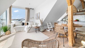 Een moderne woonkamer met een groot raam, een bank, een eethoek en een keuken.