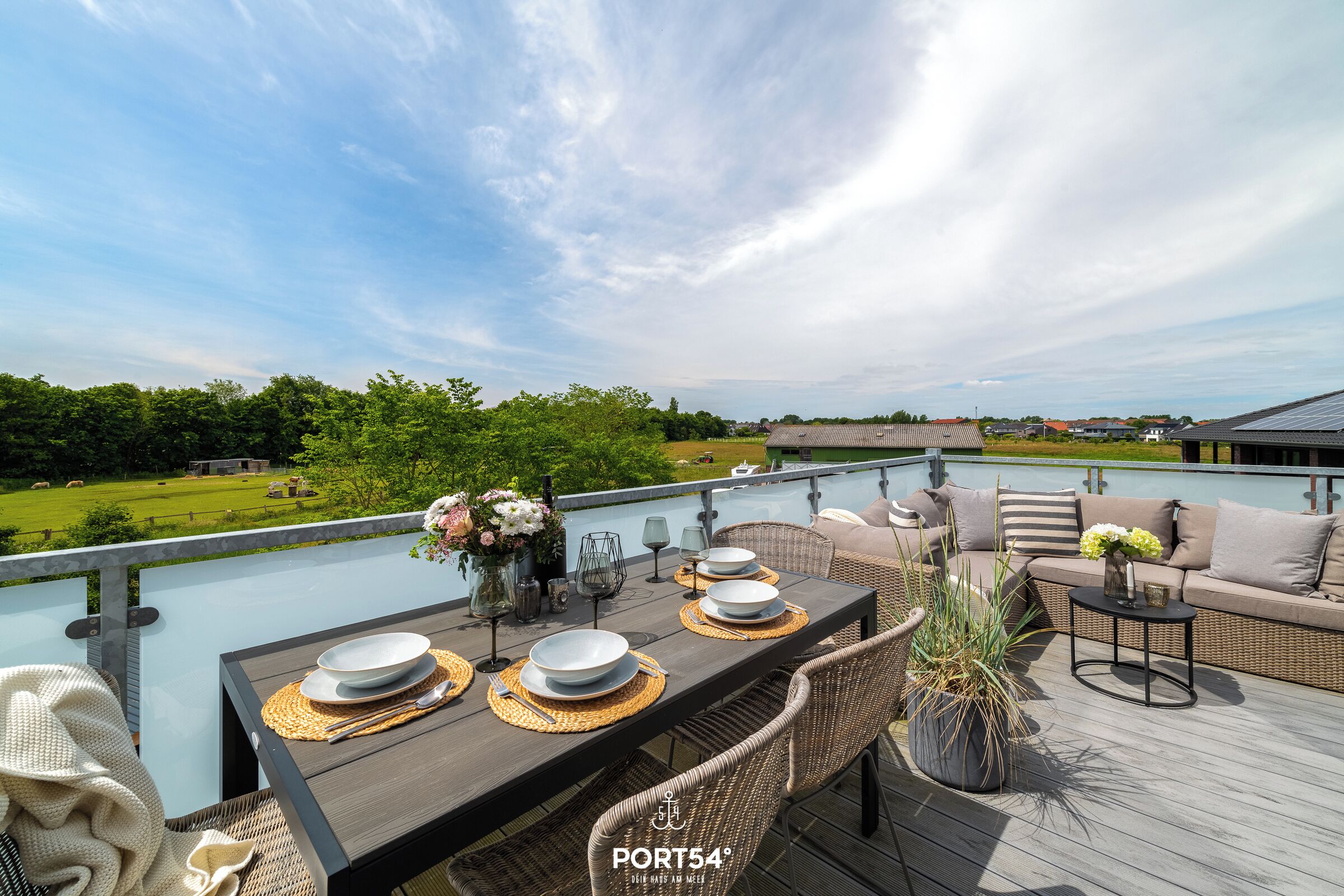 A deck with a dining table set for four, outdoor furniture, and a view of the landscape.