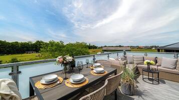 A deck with a dining table set for four, outdoor furniture, and a view of the landscape.