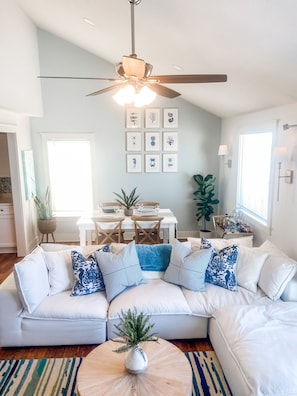 A modern living room with a white sectional sofa, a dining table with chairs, a ceiling fan, and framed artwork on the wall. - Oceanfront | Sunset Balcony | Pet-Friendly (Port St. Joe)