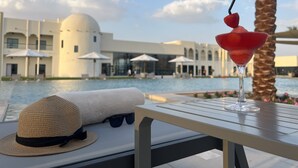 Escena junto a la piscina con una bebida en copa de martini, una pajita y un sombrero de paja sobre una mesa.