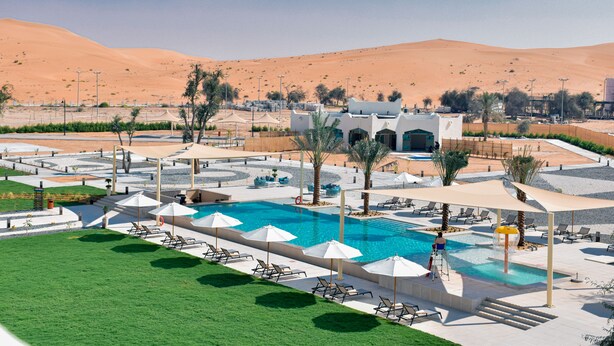 Zona de piscina en un resort con sillones de descanso y sombrillas, rodeada de colinas desérticas.