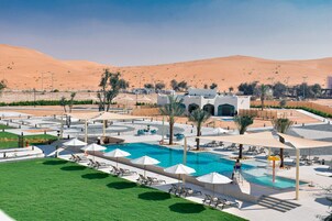 Área de piscina do resort com espreguiçadeiras e guarda-sóis, rodeada por colinas no deserto.