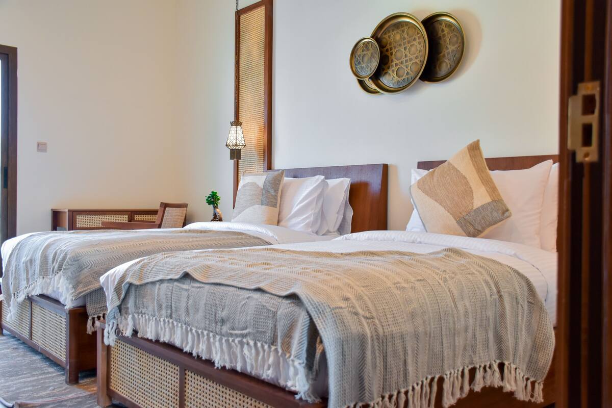 A hotel room with two beds, a woven headboard, a wall-mounted decorative plate, and a hanging lamp.
