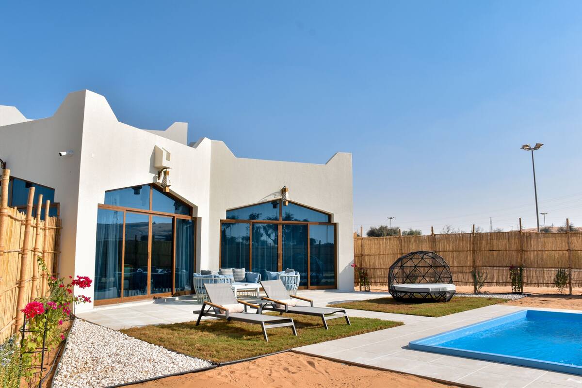 A modern house with a swimming pool, outdoor seating, and a large glass door.