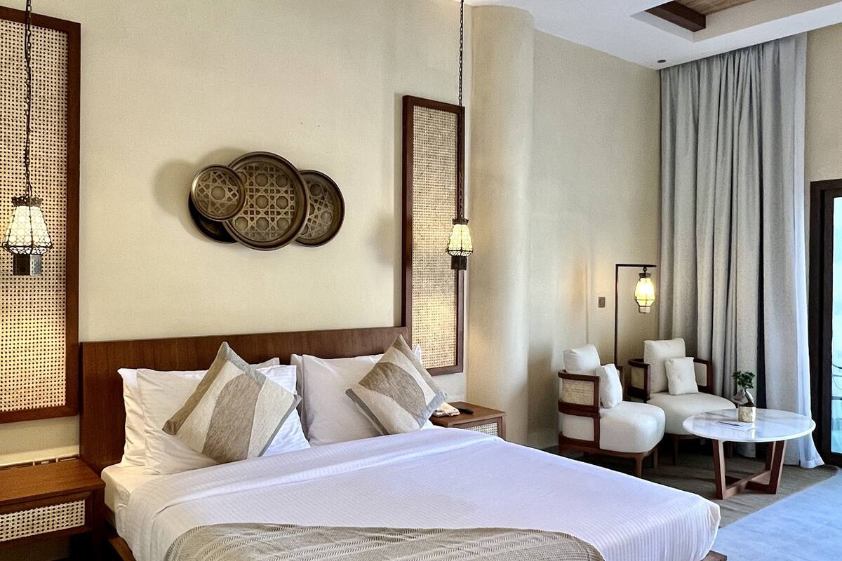 A spacious hotel room with a large bed, a sitting area with two chairs, a small table, and a decorative wall piece.