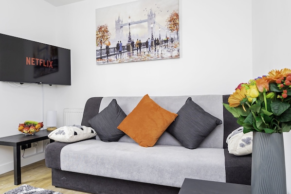 Una sala moderna con un sofá gris, un televisor negro y un cuadro de un puente.