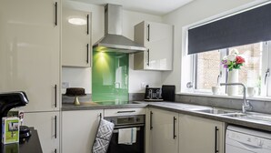 Une cuisine moderne avec des meubles blancs, un four encastré, un lave-vaisselle et une fenêtre donnant sur un immeuble en briques.