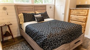 A bedroom with a bed, wooden headboard, a nightstand, and a dresser.