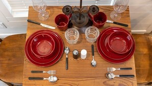 A wooden dining table set with red plates, clear glasses, and cutlery.