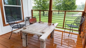 A wooden deck with a rustic table and metal chairs, overlooking a grassy area.