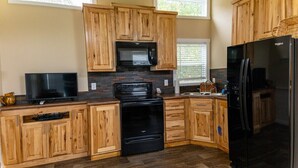 A kitchen with wooden cabinets, a black microwave, a stove, a refrigerator, and a television.
