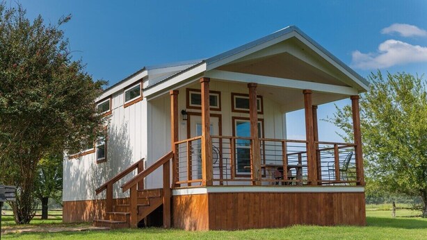 A two-story building with a covered porch, wooden steps, and a view of the surrounding landscape.