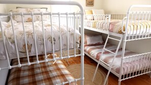 A bunk bed with a checkered bench in front, a floral bedspread, and a small rug on the wooden floor. - Sunset Meadows in Sunset Strip (Sunset Strip)