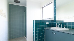 A bathroom with teal tiles, a white sink, and a window with blinds. - Sunset Meadows in Sunset Strip (Sunset Strip)