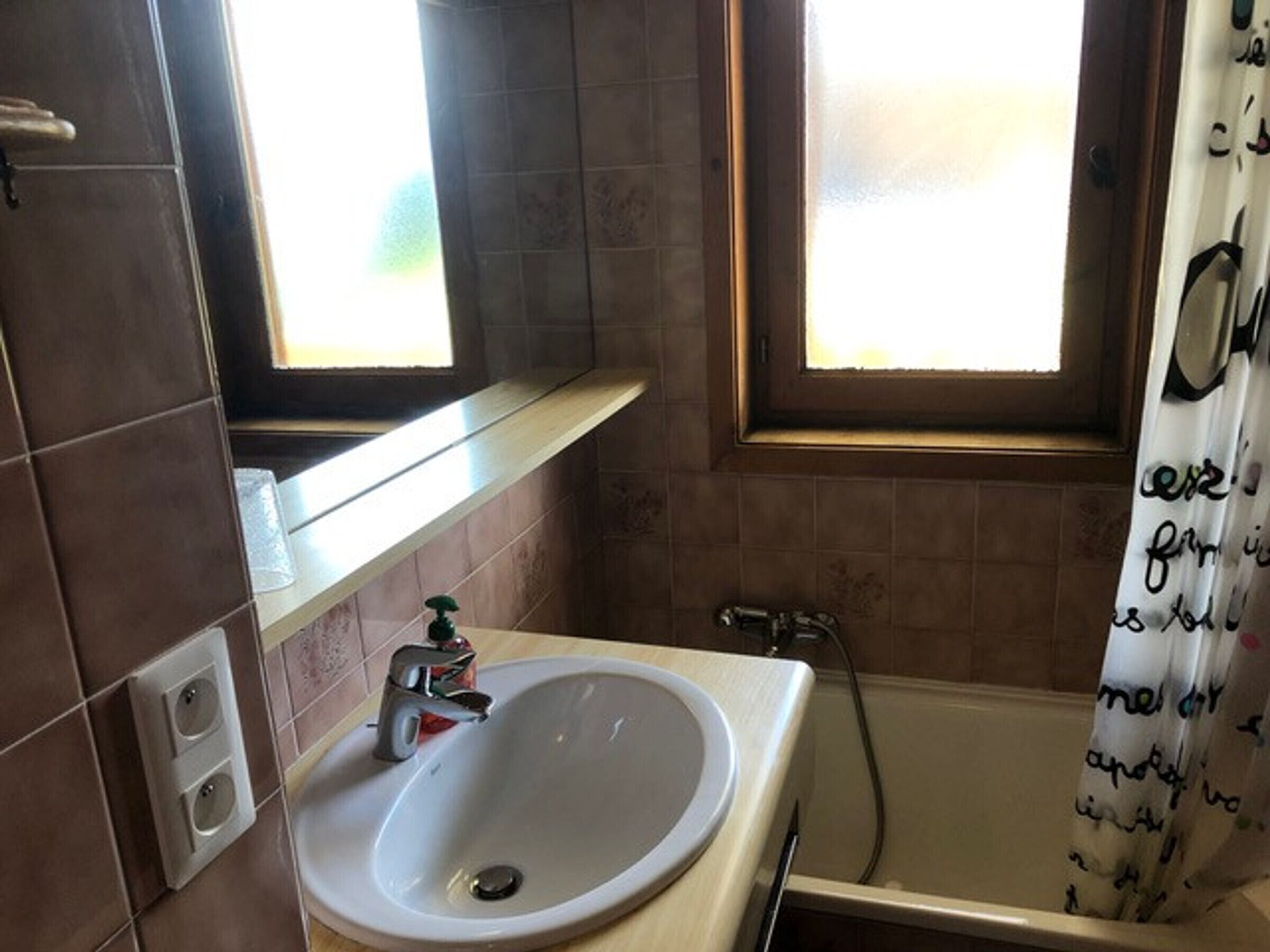A bathroom with a sink, faucet, and a shower curtain with text.