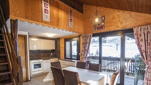 A wooden interior with a dining table, chairs, a kitchen, and a balcony with a railing. - Cozy 3-room apt, 7 pers, near cable car (Châtel)