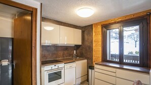 A compact kitchen with white cabinets, a built-in oven, and a window with a view of the outside. - Cozy 3-room apt, 7 pers, near cable car (Châtel)
