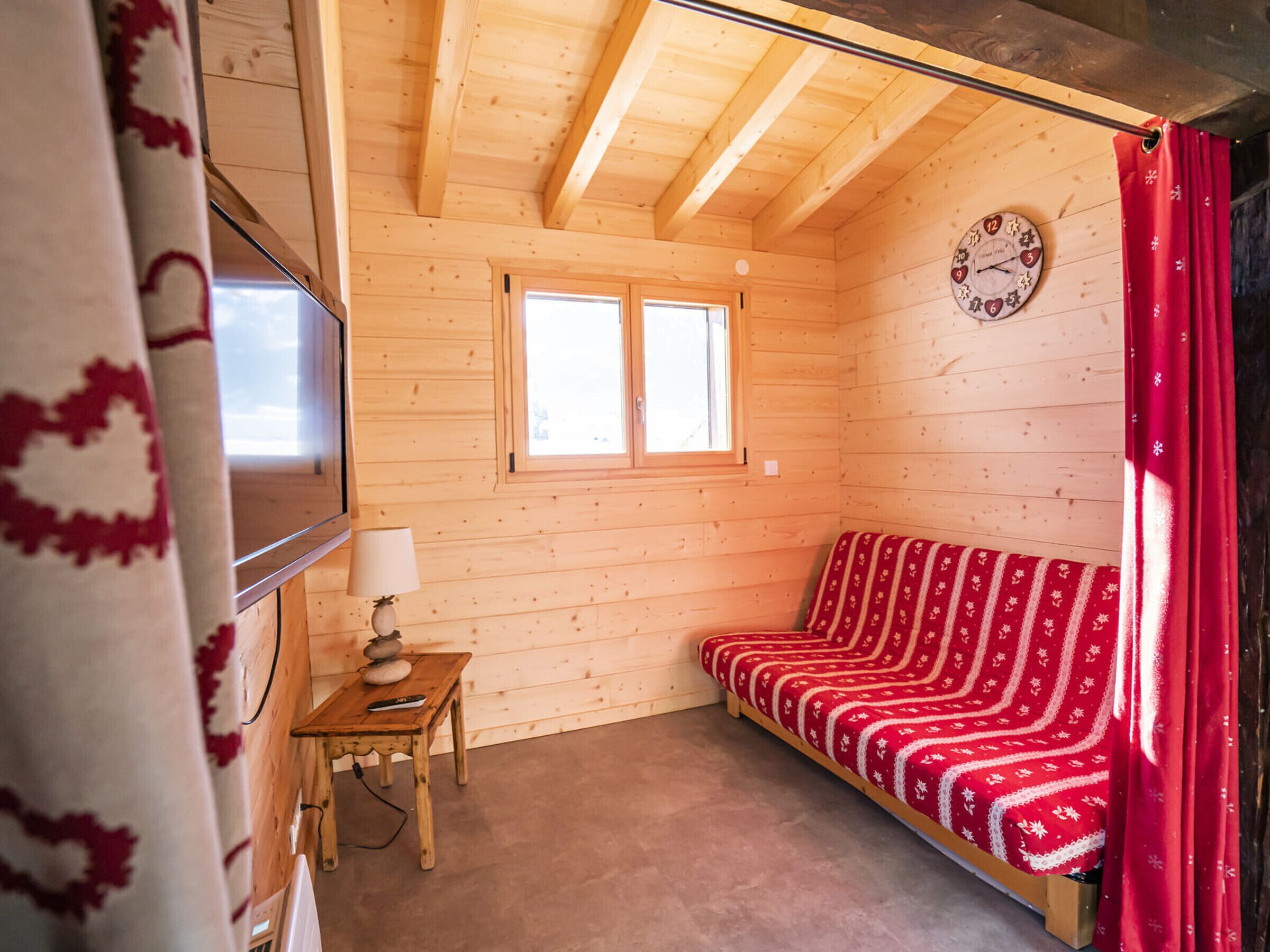 A wooden cabin interior with a sofa, a table with a lamp, and a clock on the wall.