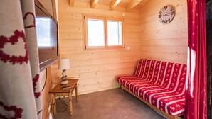 A wooden cabin interior with a sofa, a table with a lamp, and a clock on the wall. - Cozy 3-room apt, 7 pers, near cable car (Châtel)