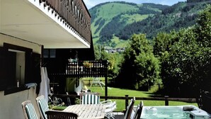 A wooden deck with a hot tub, outdoor seating, and a view of green hills. - Charming chalet 8 pers, fireplace, jacuzzi, parking (Châtel)