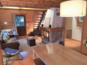 A cozy cabin interior with a fireplace, wooden walls, a sofa, a chair, and a table.