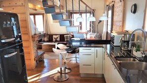 A modern kitchen with a black refrigerator, white cabinets, and a stainless steel sink. There is a dining area with a table and chairs, and a staircase leading to an upper level. - Charming chalet 8 pers, fireplace, jacuzzi, parking (Châtel)