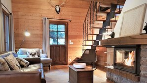 A cozy log cabin interior with a fireplace, a sofa, a chair, and a staircase. - Charming chalet 8 pers, fireplace, jacuzzi, parking (Châtel)