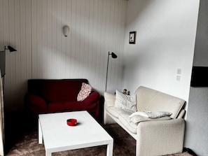 A room with a red sofa, a beige sofa, and a white coffee table. - Cozy 3-Bedroom Chalet for 6 in Châtel, Near Lifts, WiFi, BBQ, Parking, Baby Essentials (Châtel)