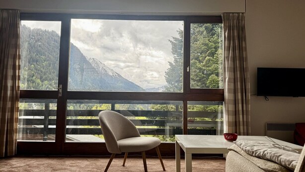 Une pièce avec une grande fenêtre, une chaise, une table et un canapé.