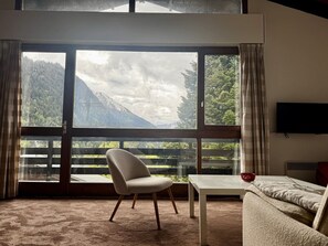 A room with a large window, a chair, a table, and a sofa. - Cozy 3-Bedroom Chalet for 6 in Châtel, Near Lifts, WiFi, BBQ, Parking, Baby Essentials (Châtel)