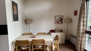 Une salle à manger avec une table dressée pour quatre personnes, deux chaises de chaque côté, un buffet blanc et une fenêtre avec des rideaux.