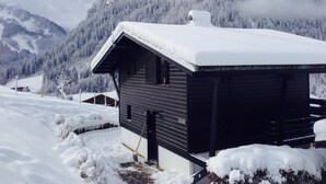 Une cabane dotée d’un toit en pente et d’une cheminée, entourée d’arbres et de montagnes couverts de neige.