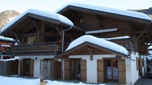A wooden chalet with a balcony and a covered entrance, surrounded by snow. - 8-room chalet, 16 pers, near village, parking, WiFi, pets allowed (Châtel)