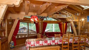 A cozy wooden cabin with a dining area featuring a table set for four, a bench, and a view of a forested area through large windows. - 8-room chalet, 16 pers, near village, parking, WiFi, pets allowed (Châtel)