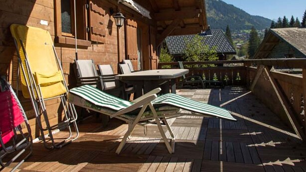 A wooden deck with a table and chairs, a yellow folding chair, and a view of mountains. - 8-room chalet, 16 pers, near village, parking, WiFi, pets allowed (Châtel)