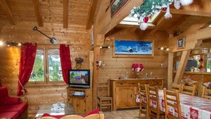 A cozy log cabin interior with a wooden dining table, chairs, a television, and a red sofa. - 8-room chalet, 16 pers, near village, parking, WiFi, pets allowed (Châtel)
